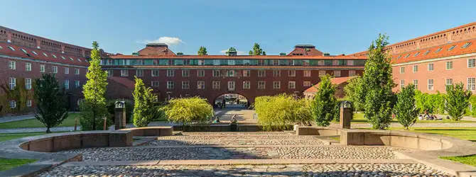 Tegelbyggnad med omgivande stor yta och grönska.