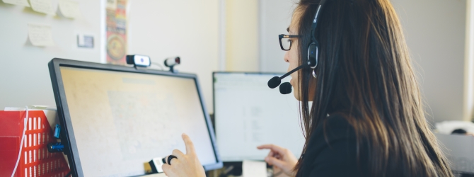 Kvinna bakifrån som tittar på en skärm och har headset på sig.